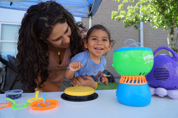 A one-year-old boy plays with an adapted bubble machine while his mom holds him
