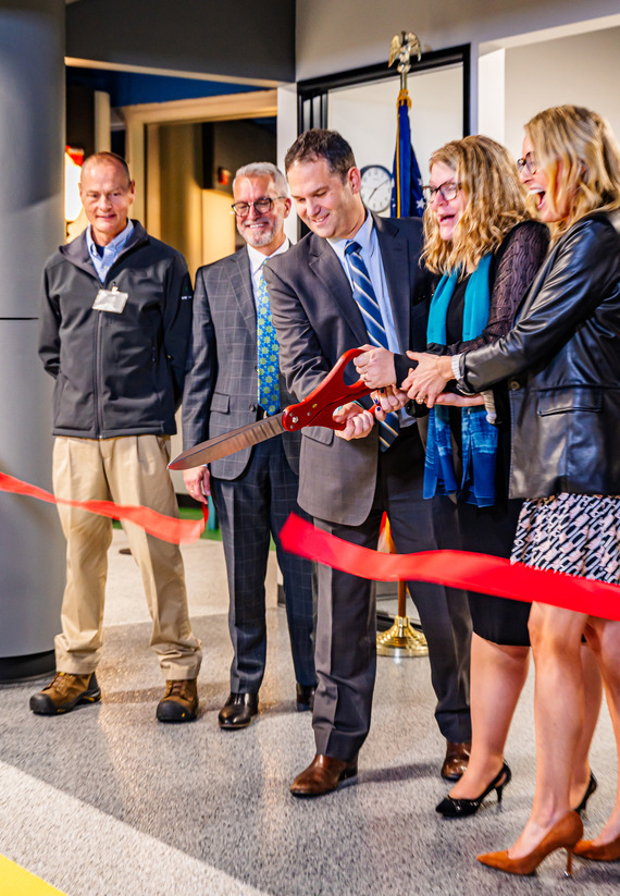 group of people cut a grand opening red ribbon with enlarged scissors