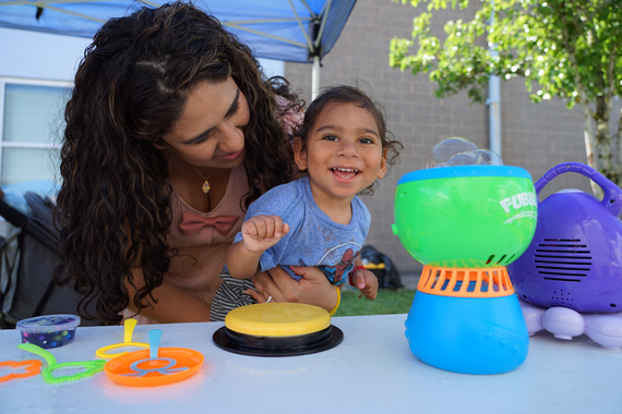 a toddler uses a switch to play with a bubble machine as his mom holds him