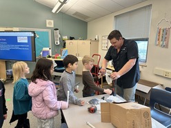 1st grade students sit and observe a plumber as he presents for career kits
