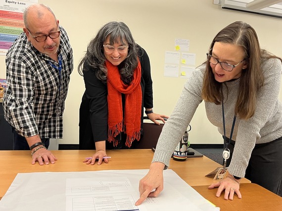 Three people lean over a table looking at poster paper