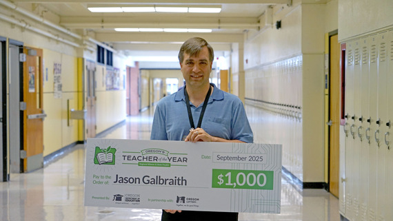 a teacher holds up an oversized check in a hallway