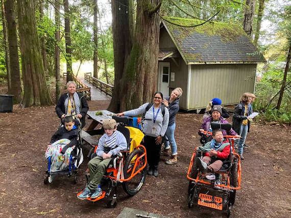 students using adaptive wheelchairs and their teachers at camp