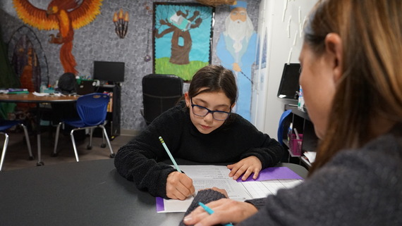 a student writes on a paper with help from a teacher