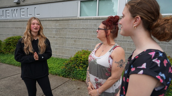 A high schooler stands with her mom and friend outside her school