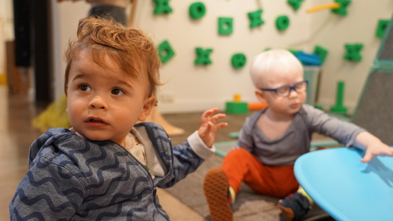 a toddler looks up while another plays in the background