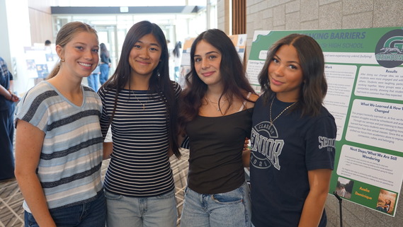 four high school women in front of posters
