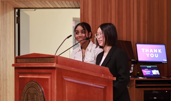 two high school women stand at a podium