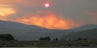 Smoke haze over hills due to wildfire, red sun breaking through