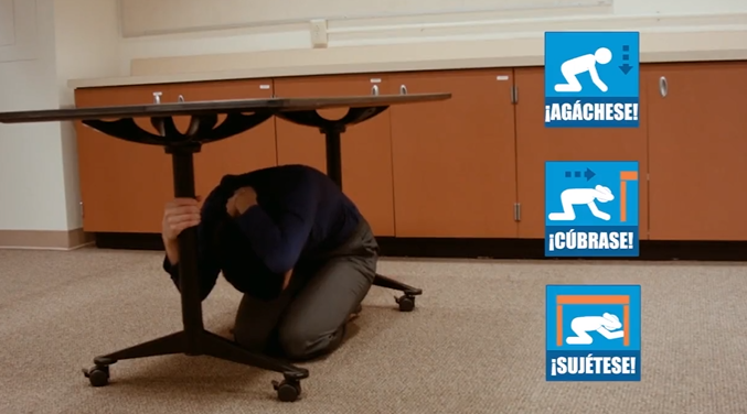Woman taking cover under a table for the Great Oregon ShakeOut, with icons in Spanish promoting Drop, Cover, Hold On