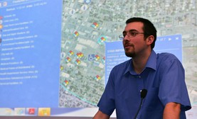 Man in blue shirt and glasses in front of digital map