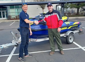 Two men shake hands in front of a jet ski