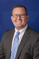 Smiling man with glasses, gray blazer, blue tie