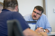 Man with moustache, brown hair listens closely to colleagues