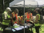 5 volunteers in orange and yellow safety vests at a table