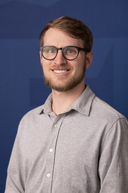 Smiling white male with brown hair, beard, moustache and black glasses wearing button down shirt