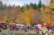 Firefighters and EMS personnel gather around several fire trucks on a fall day