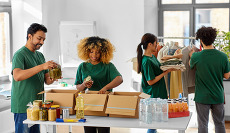 Four volunteers in green shirts pack boxes with food and sort donated clothing