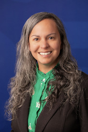 Smiling woman with long curly gray hair, black blazer, green blouse