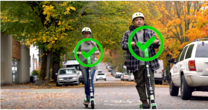 A still snapshot of two people correctly riding electric scooters.