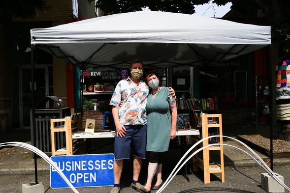 The owners of Revolutions Bookshop wear masks in front of their Healthy Businesses parking plaza.