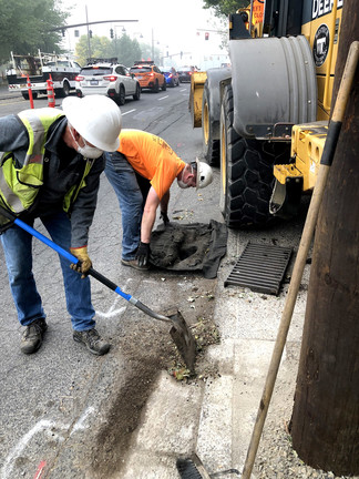 Two masked construction workers work on SW Naito Parkway