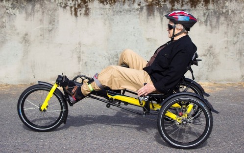 Side view of an older person riding a yellow recumbent bike with three wheels