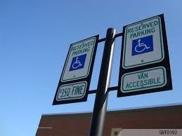 Looking up we see 2 accessible parking signs that read, “Reserved Parking,” with the icon of a person in wheelchair below the words
