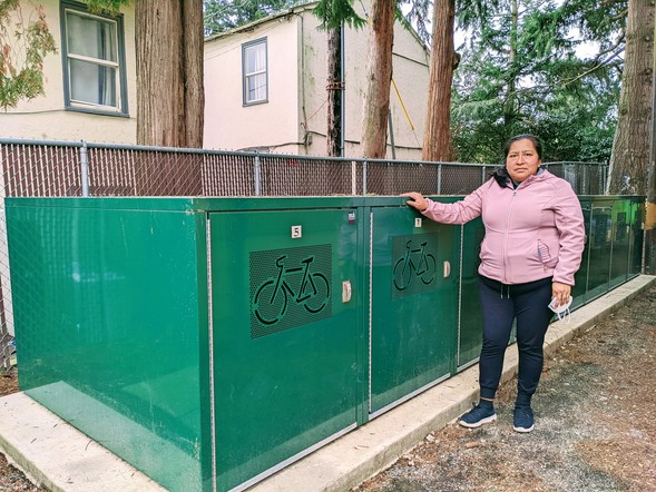 A resident at a Hacienda CDC community stands next to a row of green bike lockers outside their housing complex.
