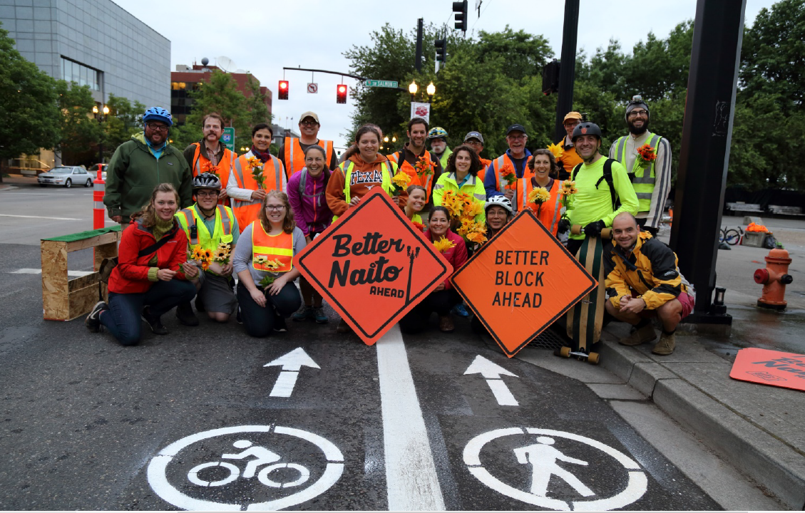 Better Block PDX volunteers in 2015 dressed in high-visibility vests, holding two road signs that read “Better Naito Ahead” and “Better Block Ahead”