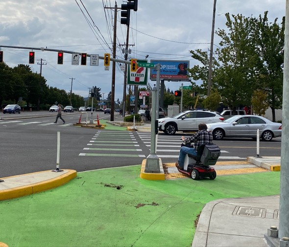 Person uing mobility device waits for signal to change at a new protected intersection on SE Division Street at 148th in September 2022