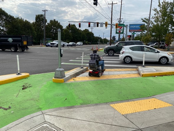 Person uses a mobility device to safely wait for the traffic signal to change at a protected intersection on Division at 148th September 2022