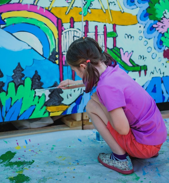 An elementary-aged child in pigtails help paint a colorful mural.