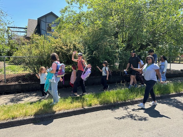 A group of Transportation Academy high school students walking with younger elementary school-aged students on a sidewalk on a sunny day. 