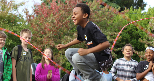 A student jumping between two jump ropes playing Double Dutch in front of seven of their peers wearing backpacks.