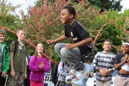 A student jumping between two jump ropes playing Double Dutch in front of seven of their peers wearing backpacks.