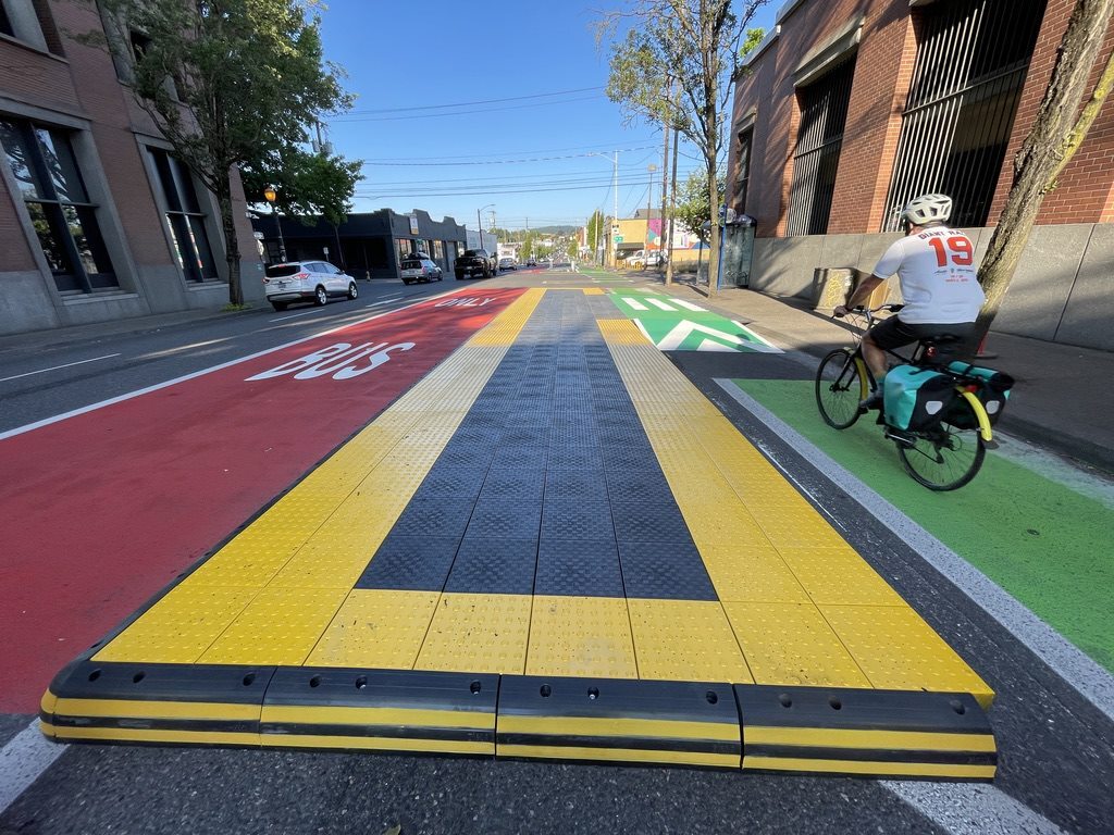 A yellow and black raised bus platform separates vehicular and bus lanes from protected bike lane on SE Hawthorne Boulevard.