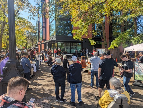 A crowd of people gather at St Johns Plaza on a beautiful fall day.