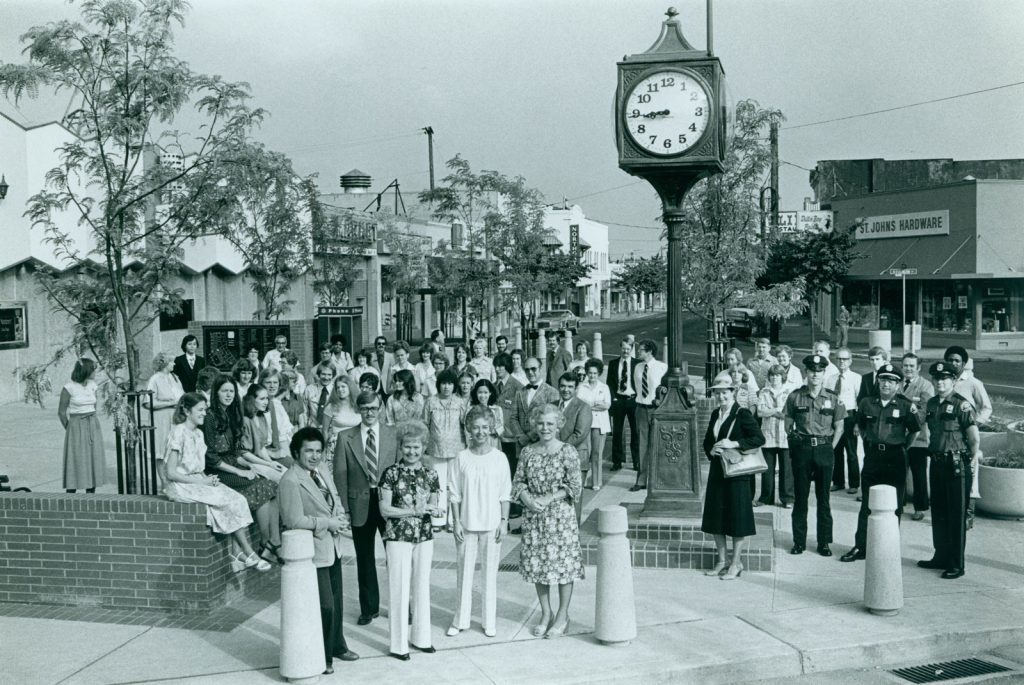 A black and white historical photo of St Johns Plaza.  A crowd of people pose in front of the plaza near the St Johns Clock to celebrate its opening.