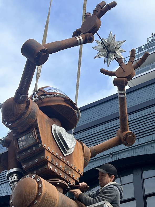The top half of a large robot sculpture.  It's hands are raised in the air with a star floating between its hands.