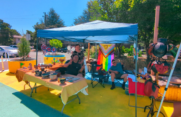Vendor sit under a pop-up tent during a market day at Arleta Triangle Square.  The street is brightly rainbow colored.