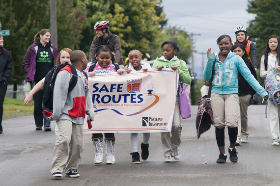 More than a dozen youth and adults walk to school on a neighborhood street and holding a Safe Routes to School banner.