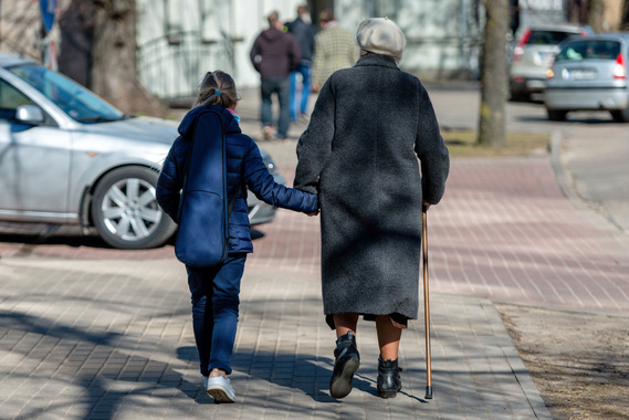 The backs of a youth and an elderly individual walking on a sidewalk hand-in-hand.