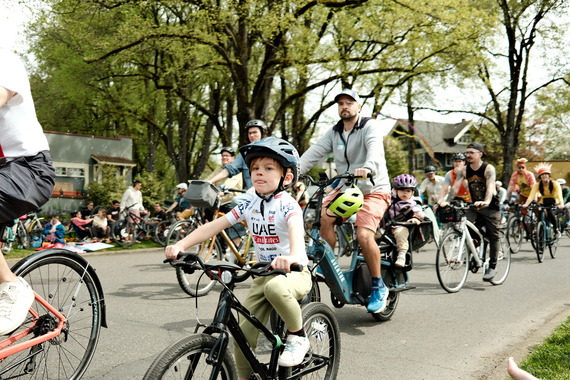 An early elementary school-aged kid riding a bike (foreground) with dozens of other people riding bicycles on a neighborhood street (background).