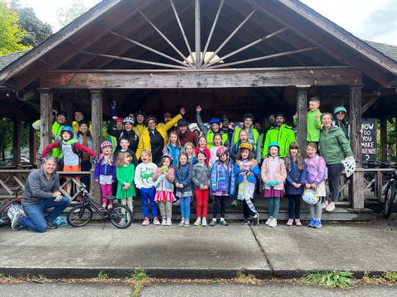 A group of more than 40 elementary school students and adults, some wearing helmets, standing together for a photo under a larger roof.