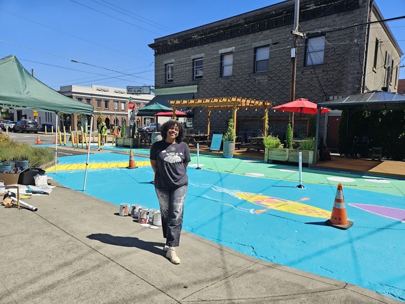 The artists who designed the street painting stands in front of the painted plaza.