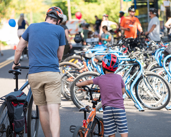 An adult and a child face away, walking with their bikes, with dozens of other bikes parked in the background.