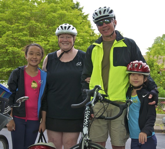 Two adults and two children stand together, smiling, with bike helmets on.