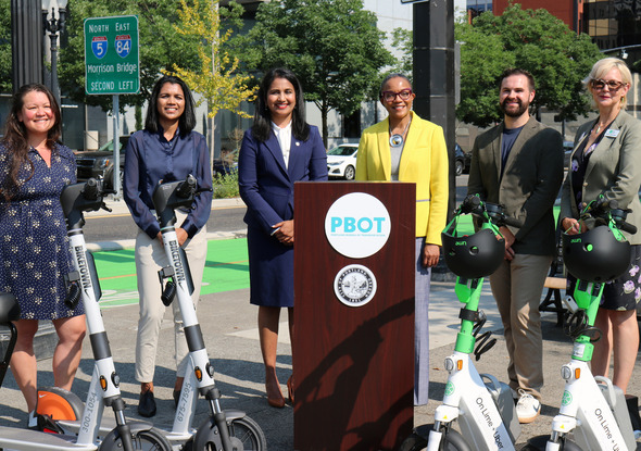 Leaders who spoke at the e-scooter press conference stand behind scooters for a group photo
