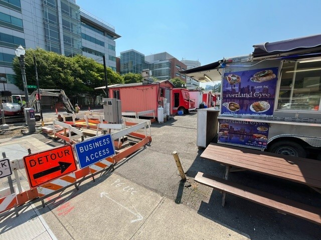 [Signs around the construction on SW Fourth Avenue say detour and business access next to a lot with several food carts.